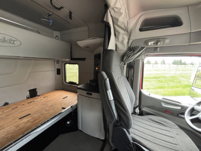 Peterbilt 579 truck interior sleeper cab with bunk bed platform and storage cabinets visible. Driver seat and dashboard seen on right.