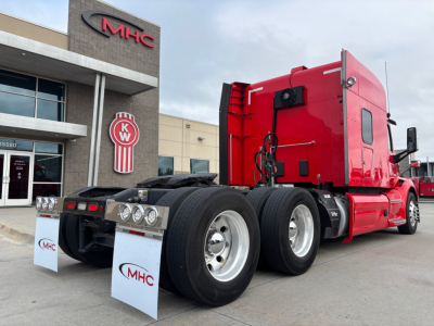 Peterbilt 579 tractor rear view showing red sleeper cab and dual rear axles with mudflaps, at MHC dealership.