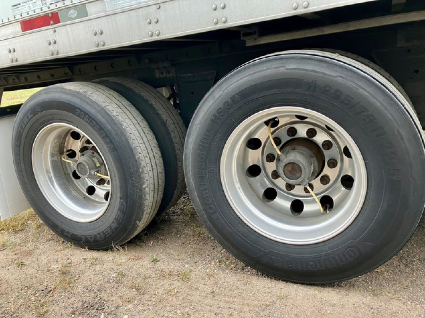 Dual rear trailer axles with big tires and rims; side of refrigerated utility trailer visible with riveted metal structure.