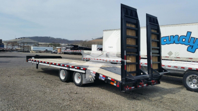 Trailer showing a flatbed with ramps in raised position; industrial yard in background; black and silver with dual axles and ramps.