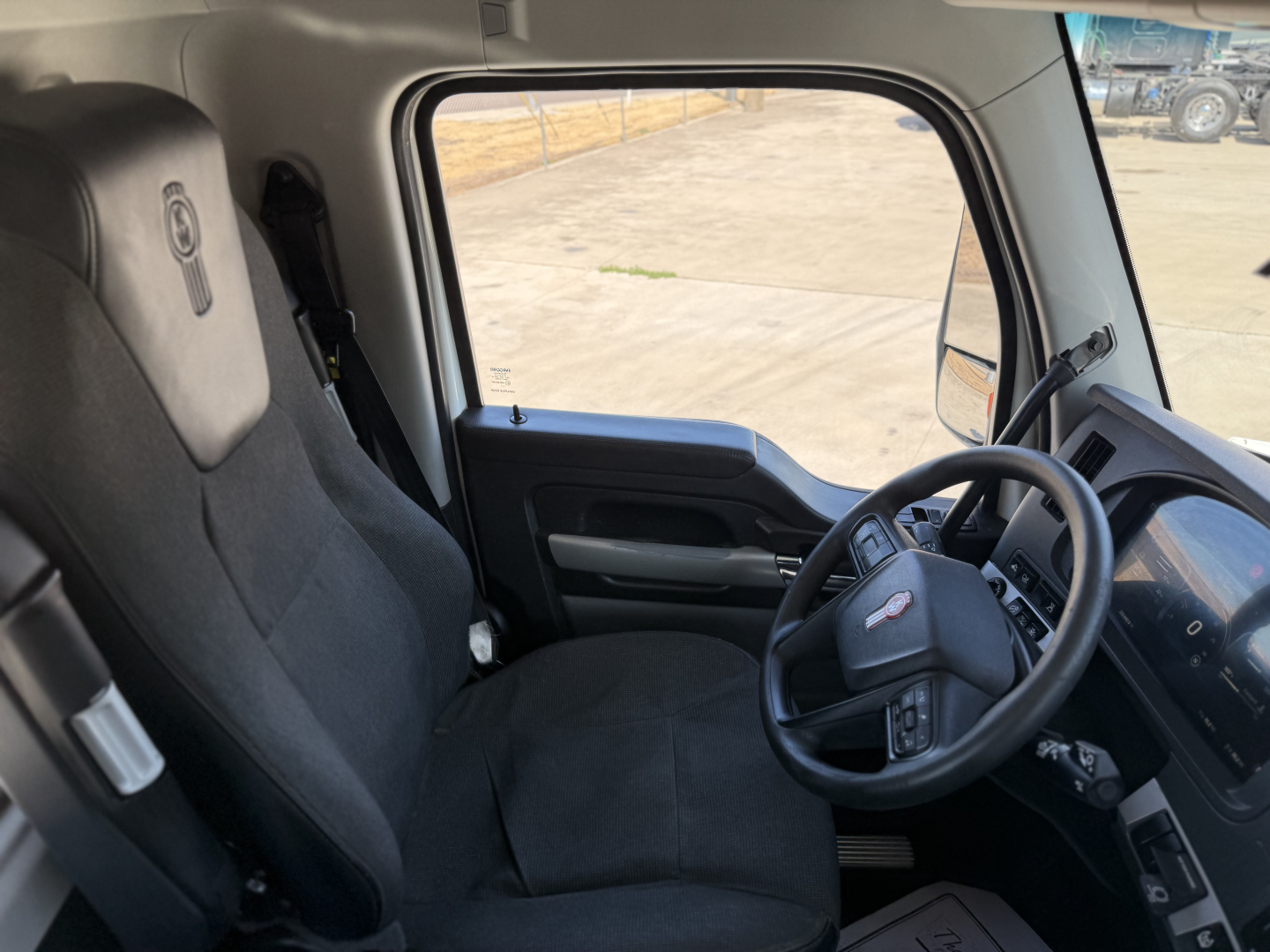 Kenworth T880 truck cabin interior showing driver's seat and steering wheel with Kenworth badge, dashboard, and side window view.