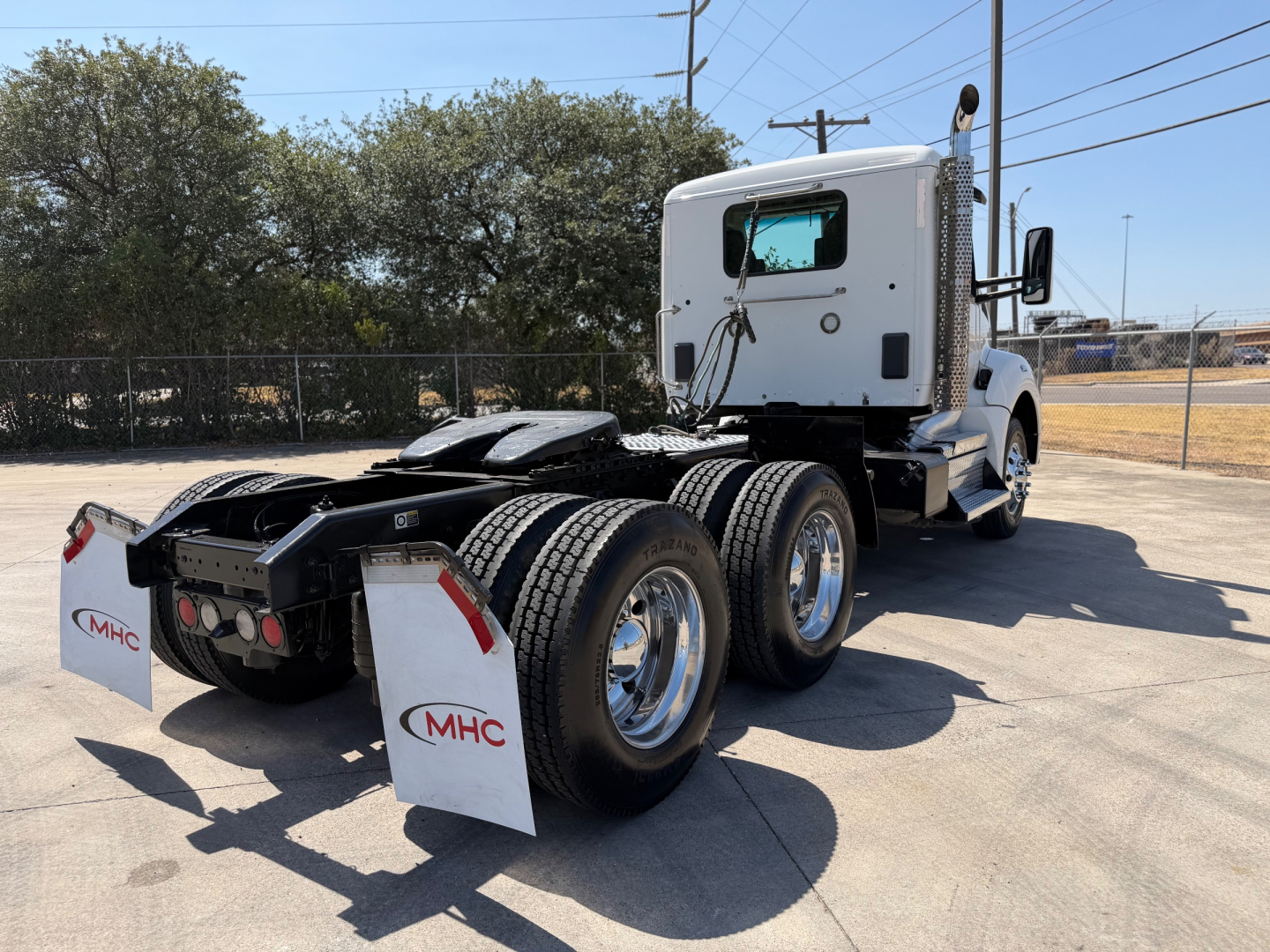 Kenworth T880 conventional daycab rear view showing dual rear axles and chassis with mud flaps and MHC logo.