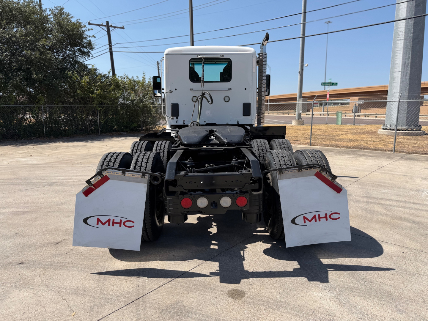 Kenworth T880 rear view showing mud flaps with MHC logo, rear bumper, and third brake lights; back of cab and dual rear axles visible.