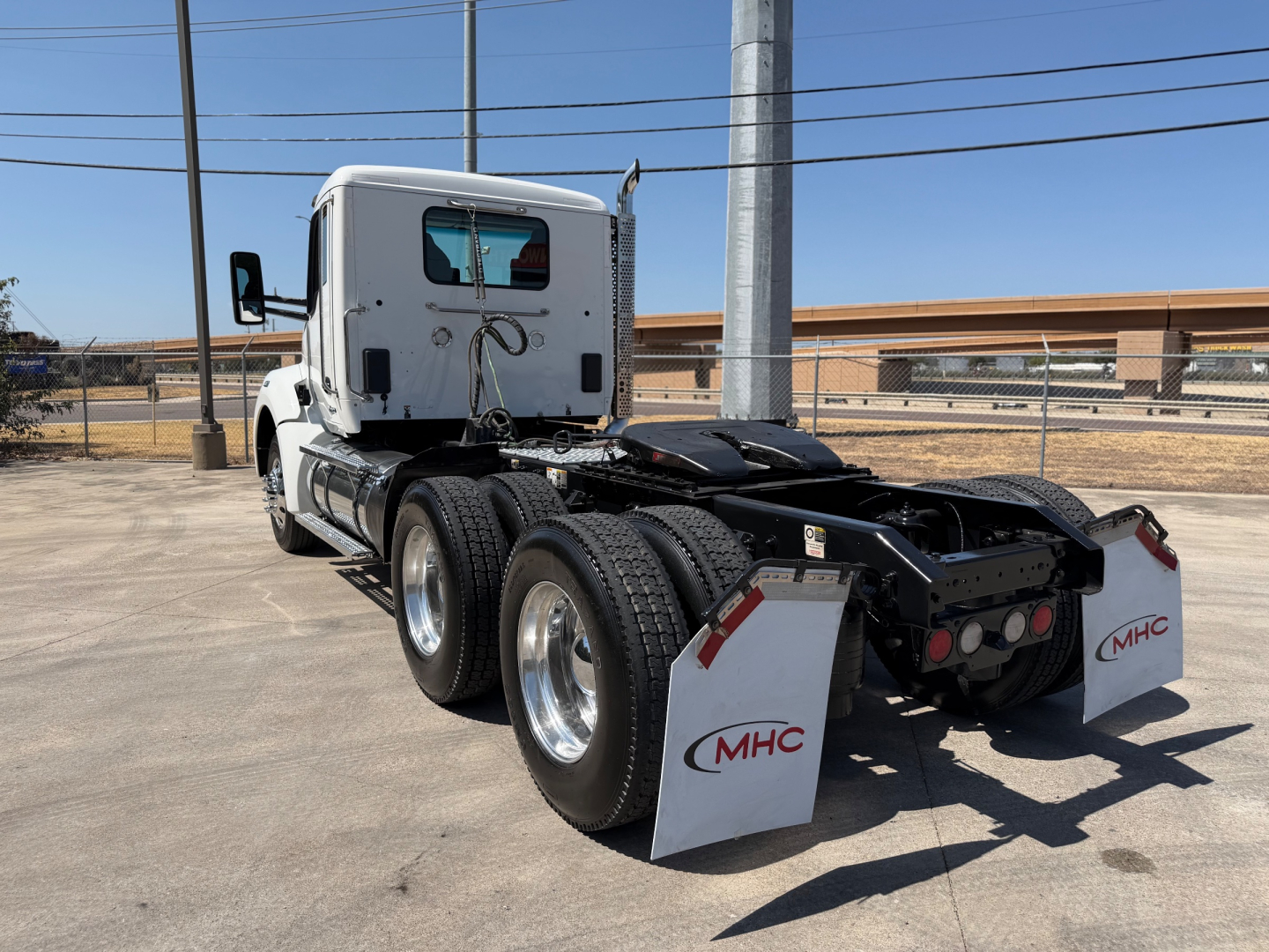 Kenworth T880 tractor rear view showing white cab, dual rear axles, and MHC mudflaps with red MHC logos.
