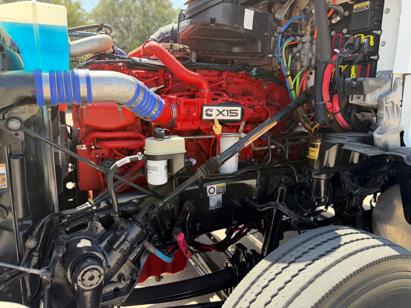 Kenworth T880 engine bay showing X15 engine badge and red engine block with various hoses, wiring, and coolant reservoir visible.