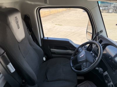 Kenworth T880 truck cabin interior showing driver's seat and steering wheel with Kenworth badge, dashboard, and side window view.