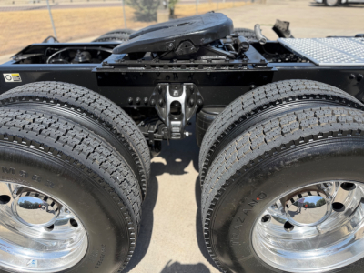 Dual rear wheels of a Kenworth truck chassis with chrome rims and tire treads visible; parts of the frame and fifth-wheel area; no readable labels besides partial tire markings.