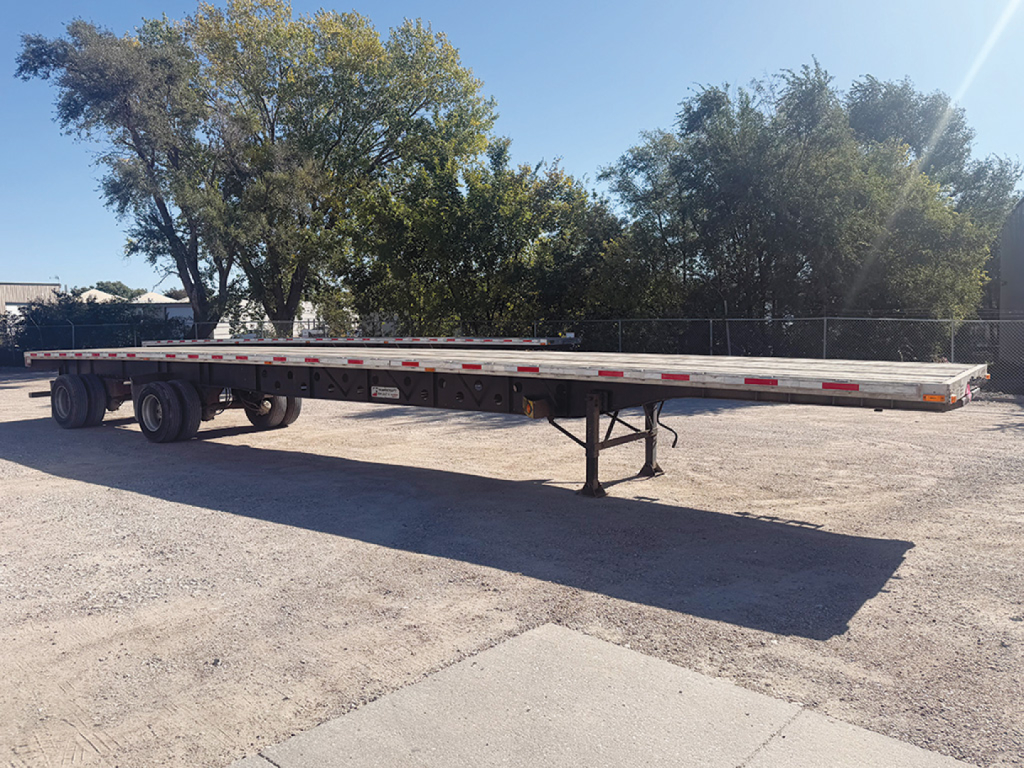 Flatbed trailer with tandem axles and support legs, long steel deck, labeled as 2006 Transcraft Eagle Super Beam.
