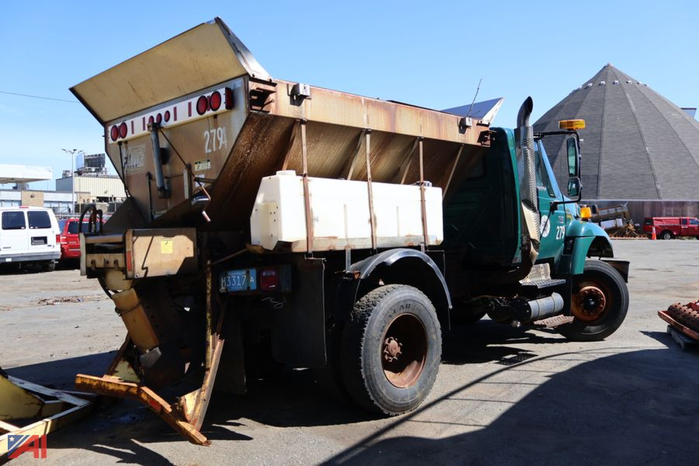 International WorkStar 7400 dump/sander truck with plow at rear, green cab, white stake body, rust on wheels, side mirror, hydraulic components visible.