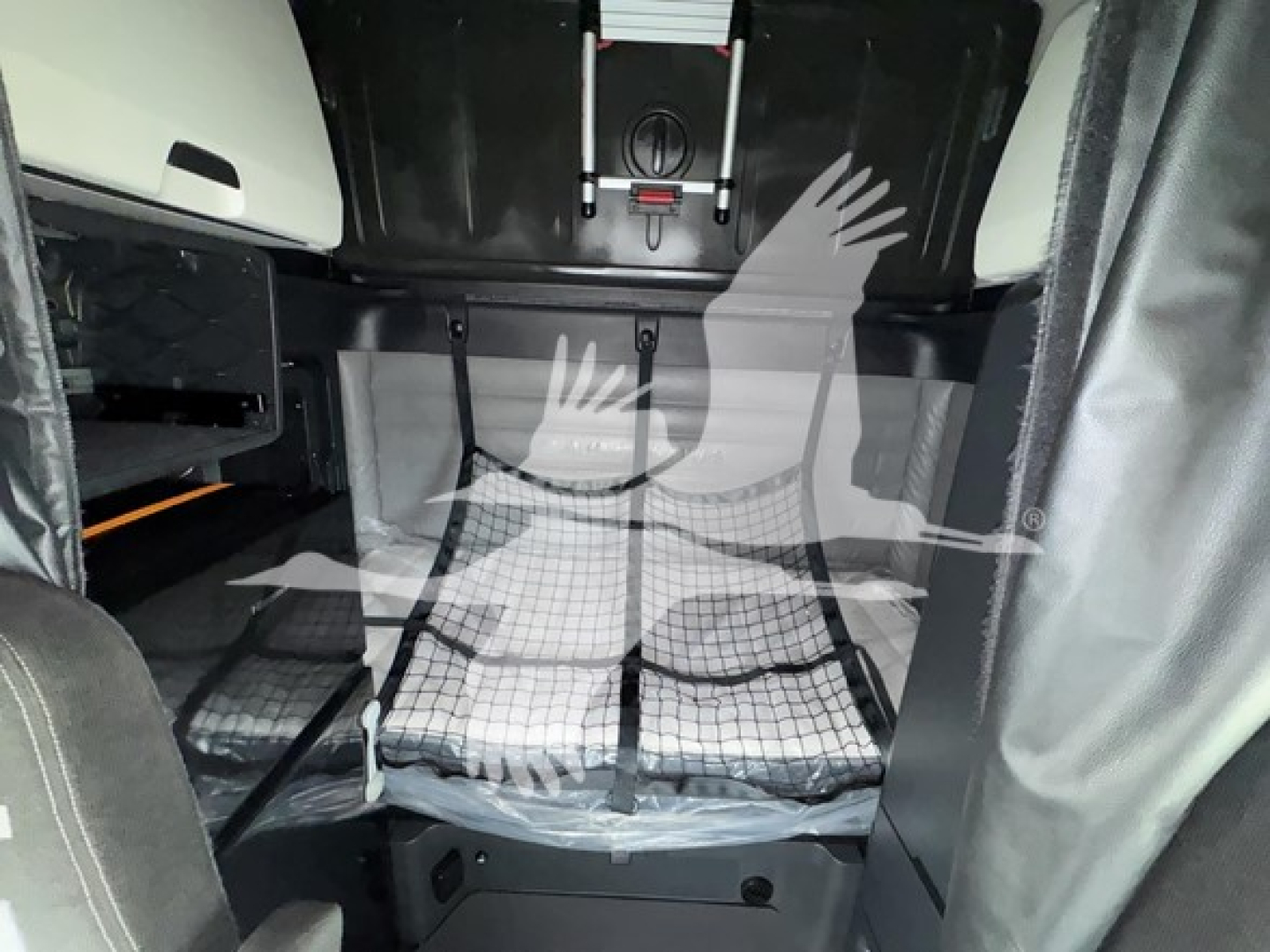 Truck cab interior showing sleeper area with netted storage and floor mat; visible straps and overhead console in Freightliner Cascadia 126 cab. Includes VIN and stock details in listing context.