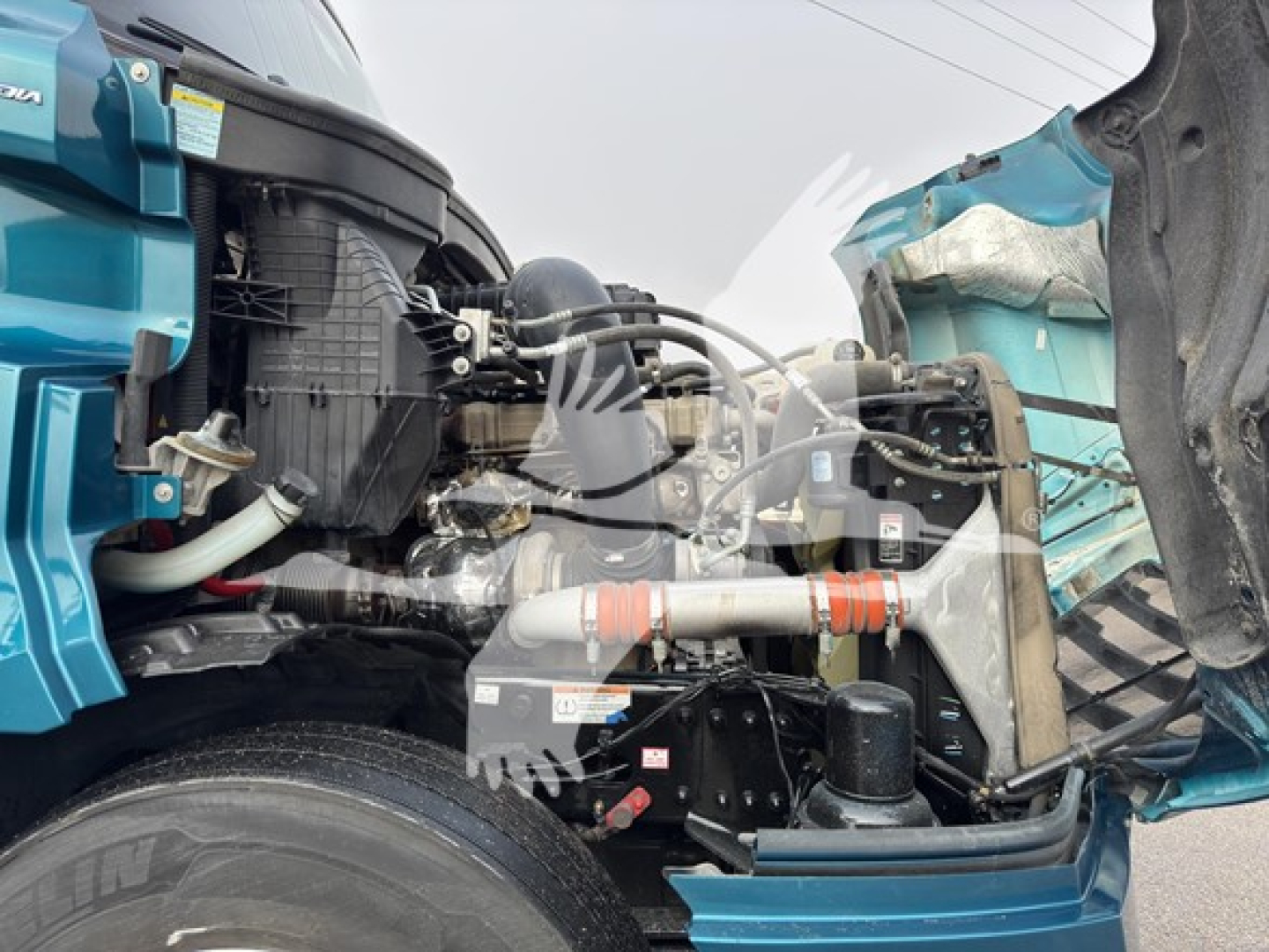 Freightliner Cascadia engine bay with exposed intake, hoses, and intercooler; front-left view showing coolant reservoir and metallic piping.