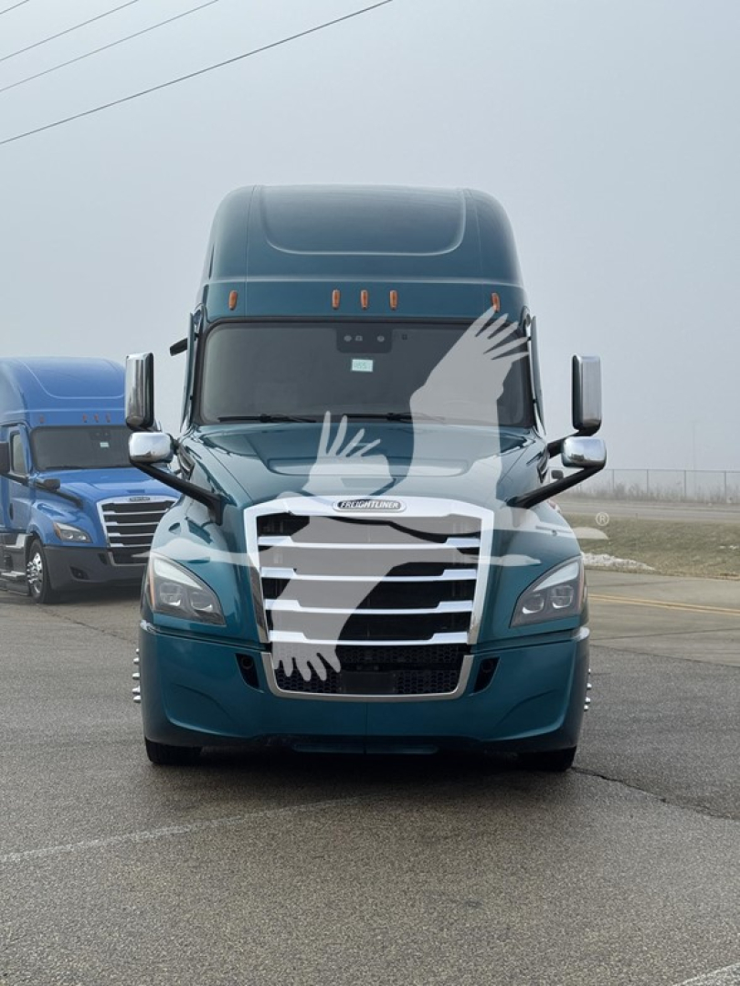 Front view of a teal Freightliner Cascadia 126 sleeper cab truck with chrome grille and blue trailer in background.
