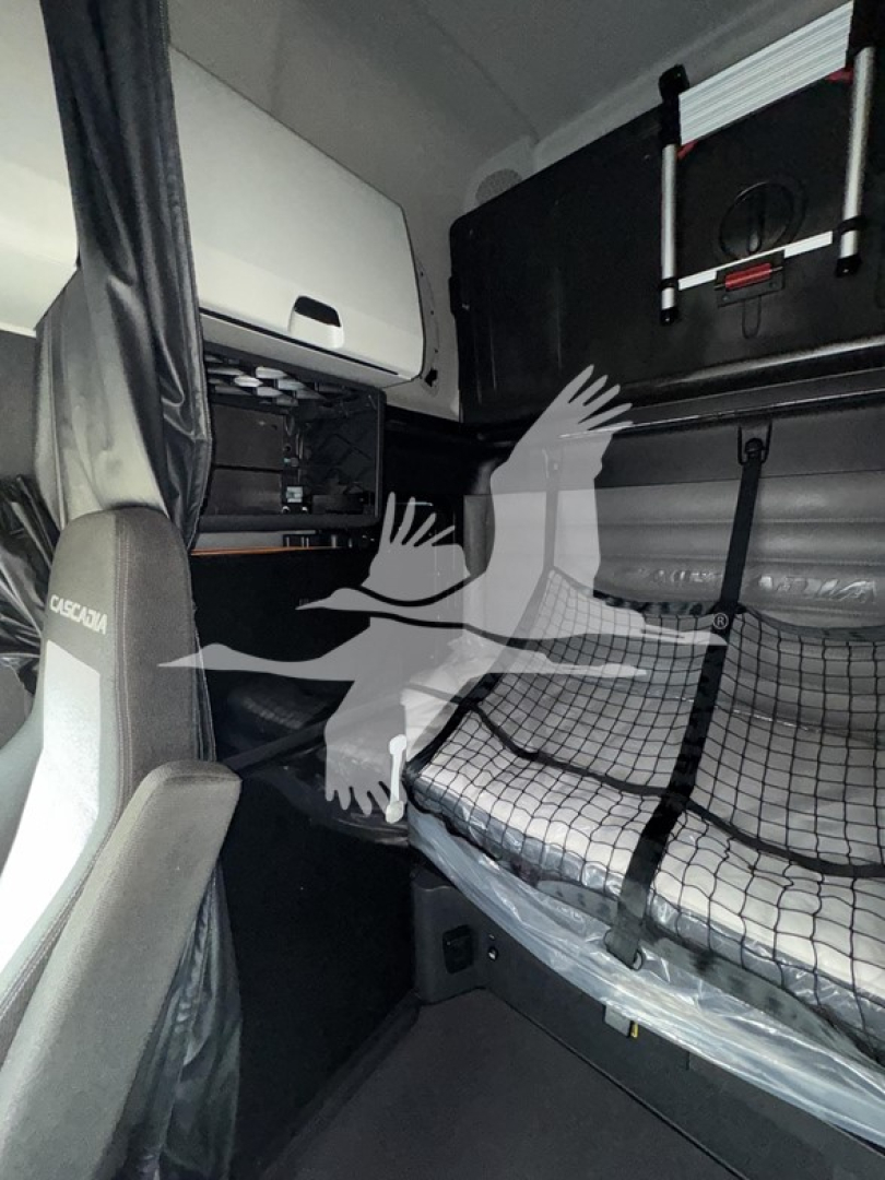 Cabin interior of a Freightliner Cascadia sleeper showing bunk bed with netting and storage, seat with 'CASCADIA' branding.