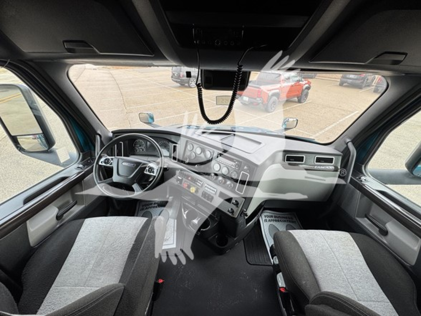 Truck cockpit interior with steering wheel, dashboard, and overhead console; no legible text visible in image.