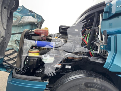 Freightliner Cascadia 126 engine bay with exposed components and wiring; blue cab color visible, coolant reservoir, hoses, and mechanical parts in view.