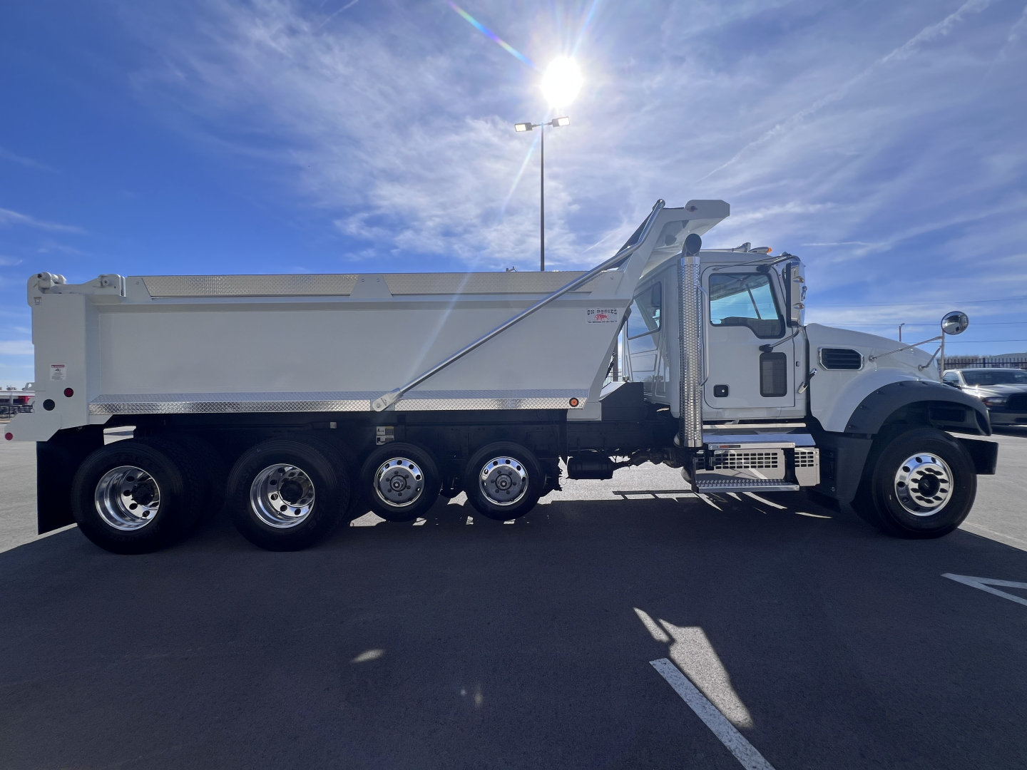 Dump truck with a white Mack GR64F dump body and multiple axles, side profile view showing the truck cab and hydraulic dump mechanisms.