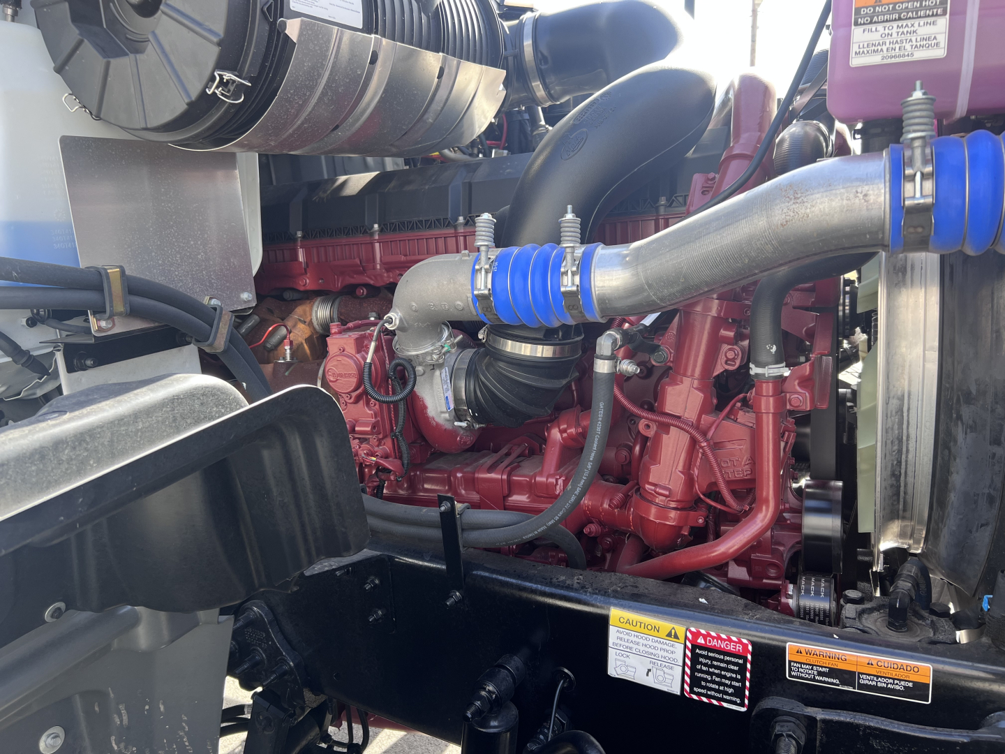 Mack GR64F engine bay showing red diesel engine with blue silicone hose fittings and surrounding components.