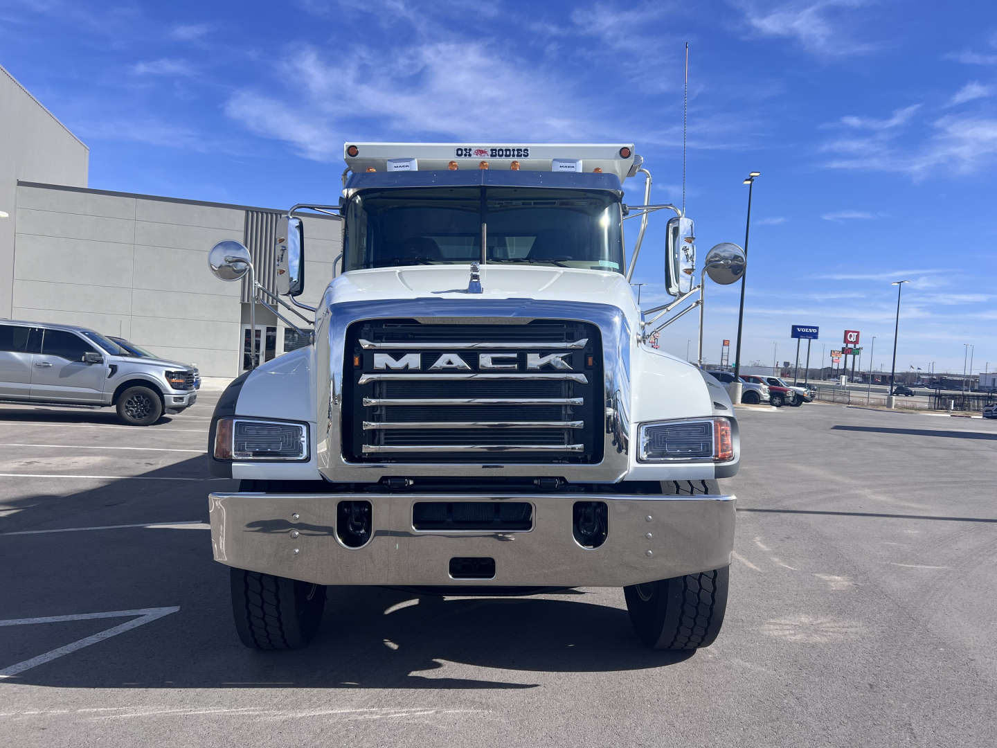 Front view of a white 2026 Mack GR64F dump truck showing large chrome grille with MACK lettering, bumper, and dual mirrors.
