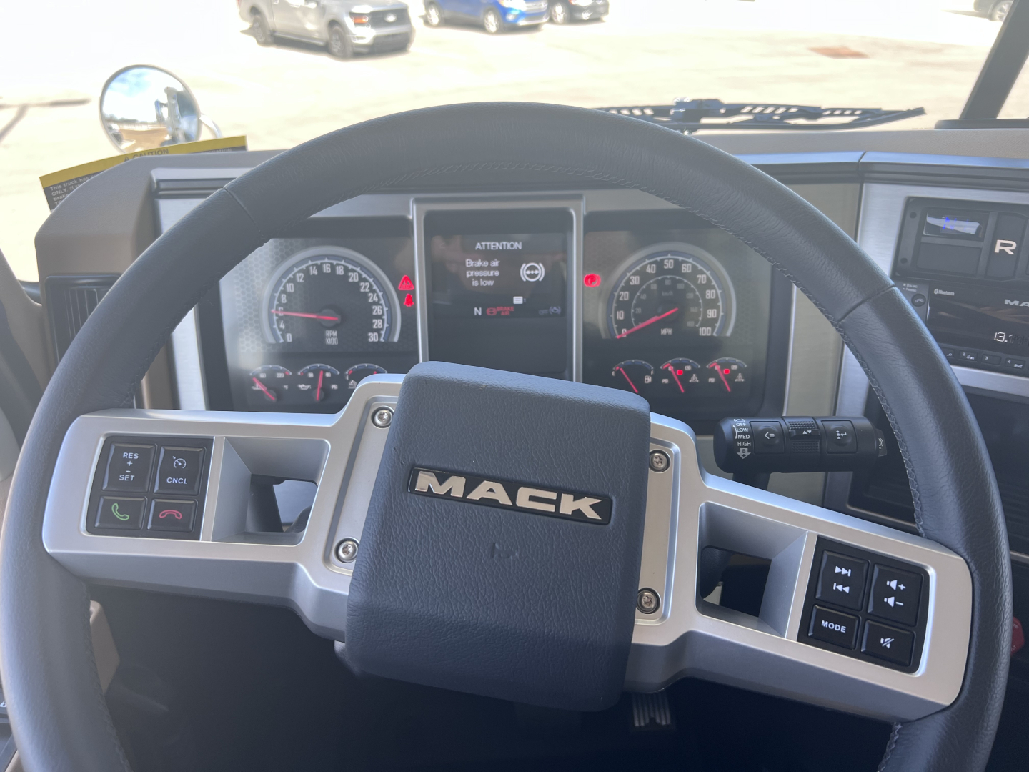 Mack GR64F cab interior showing steering wheel with Mack logo and instrument cluster, digital display, and control buttons on steering wheel.
