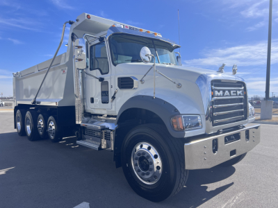 Mack GR64F dump truck front-left view showing chrome grille and dual rear axles with aluminum dump body.