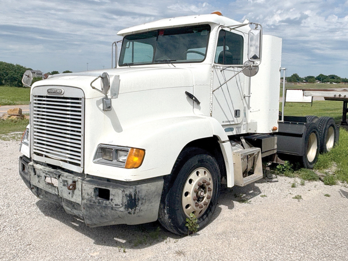 Truck front-left view of a white 1998 Freightliner FLD112 daycab with dual rear axles, showing large grille, rectangular headlights, and steps; VIN tag not visible.