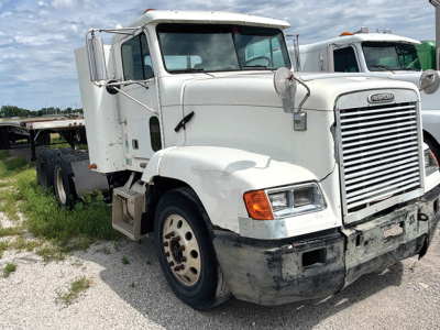 Freightliner FLD112 conventional truck front-left view showing cab, grille, and bumper with worn lower fascia, DOT mirrors, and mid-2000s styling.