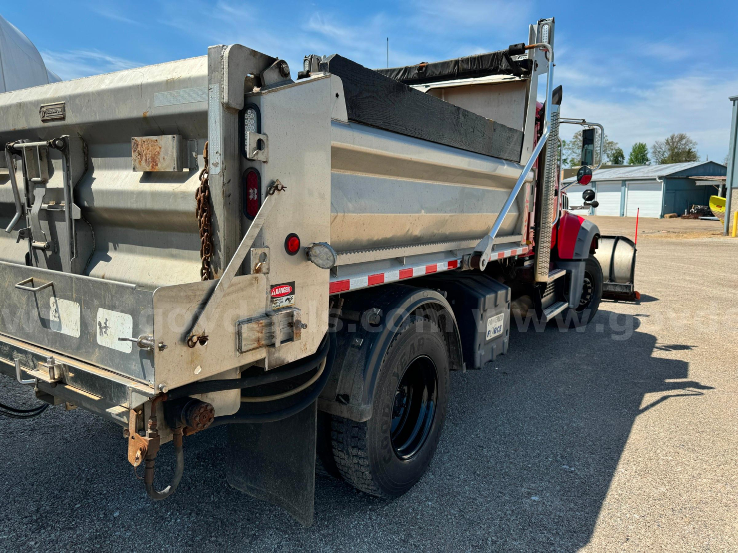 Rear/side view of a 2019 Mack Granite dump truck with dump body, dual rear wheels, reflective safety stripes, and plow category; visible VIN and stock number not on image text.