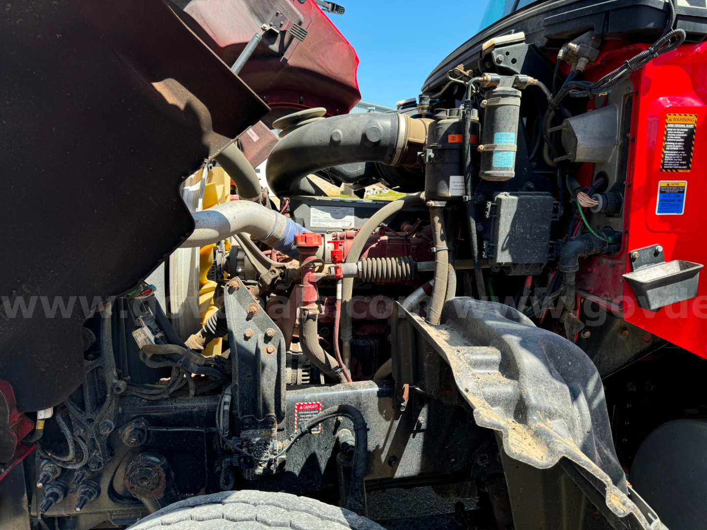 Mack Granite truck engine bay showing air intake, hoses, and components in red cab; various lines and a large black hose visible.