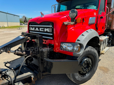 Mack Granite truck front view showing plow, red cab with black grille and bumper, large headlight assembly, tire, and AMRU badge on side.