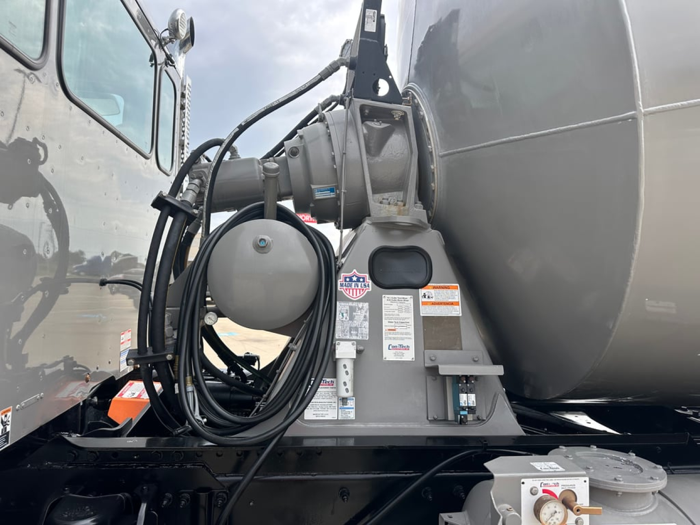 Kenworth T880 mixer truck showing front of mixer body and hydraulic hose reel with control valve and warning labels.