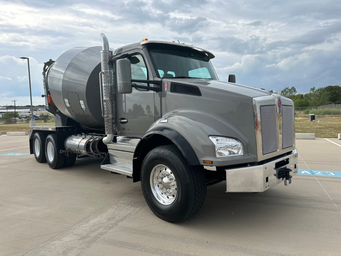 Kenworth T880 mixer truck in gray with concrete mixer, front view angled show chrome bumper, large grille, side exhaust, and dual rear axles.