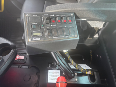 Kenworth T880 dash panel showing multiple switches and a warning label, with wiring harnesses and a red knob nearby.