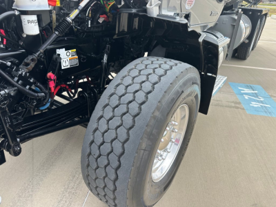 Kenworth T880 truck chassis and front tire view with wheel, suspension, and hydraulic lines visible.