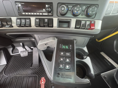 Kenworth T880 cab interior showing gear selector with N,N, R, D buttons and stack of switches on dashboard; cup holder and pedal area visible.