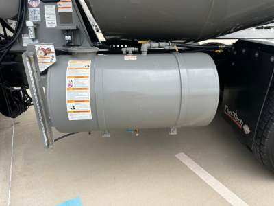 Kenworth T880 mixer truck fuel tank/air tank assembly with warning labels and mounting brackets visible under the chassis