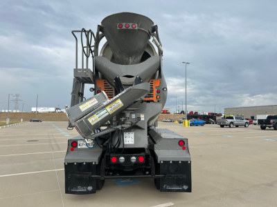 Kenworth T880 mixer truck rear showing concrete chute and rear chassis, with warning labels and hydraulic components visible.