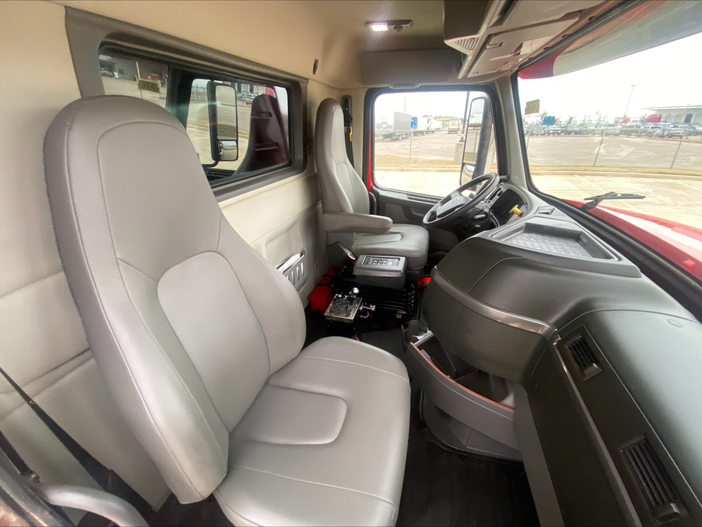 Cab interior of a Volvo VHD truck showing grey cloth seats, steering wheel, dashboard, and center console from the passenger side.