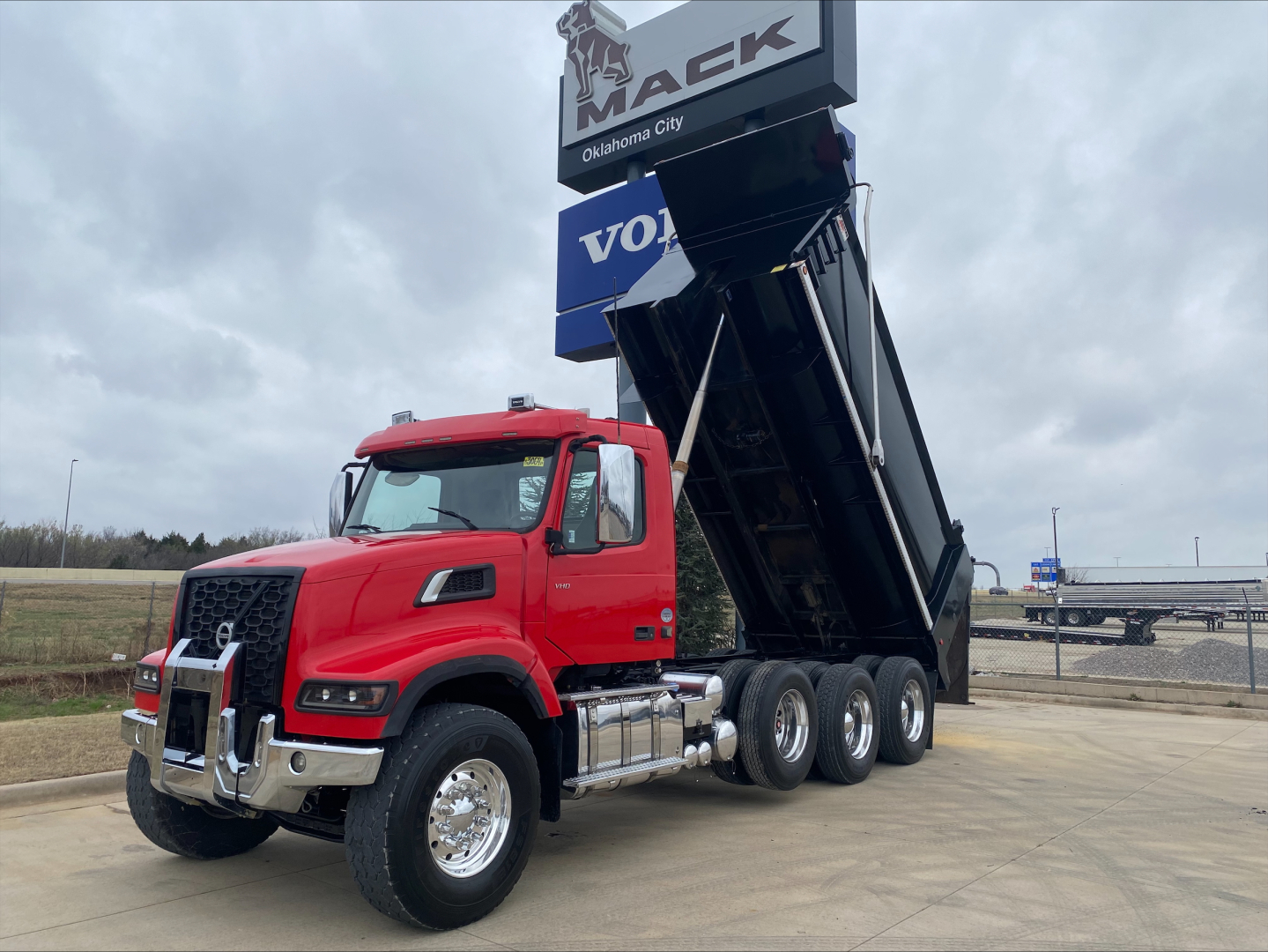 Volvo VHD dump truck with red cab and raised dump bed in a dealership lot showing Volvo Maek signage.