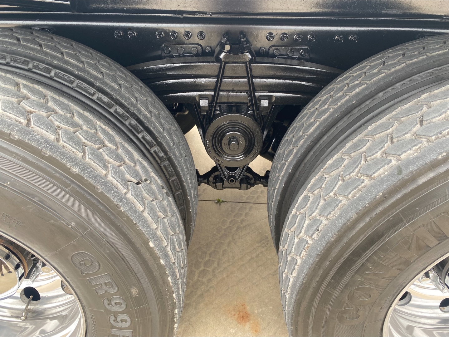 View under a Volvo VHD84F200 dump truck showing dual rear axles, leaf springs, and differential/axle housing. Visible tires and suspension components.