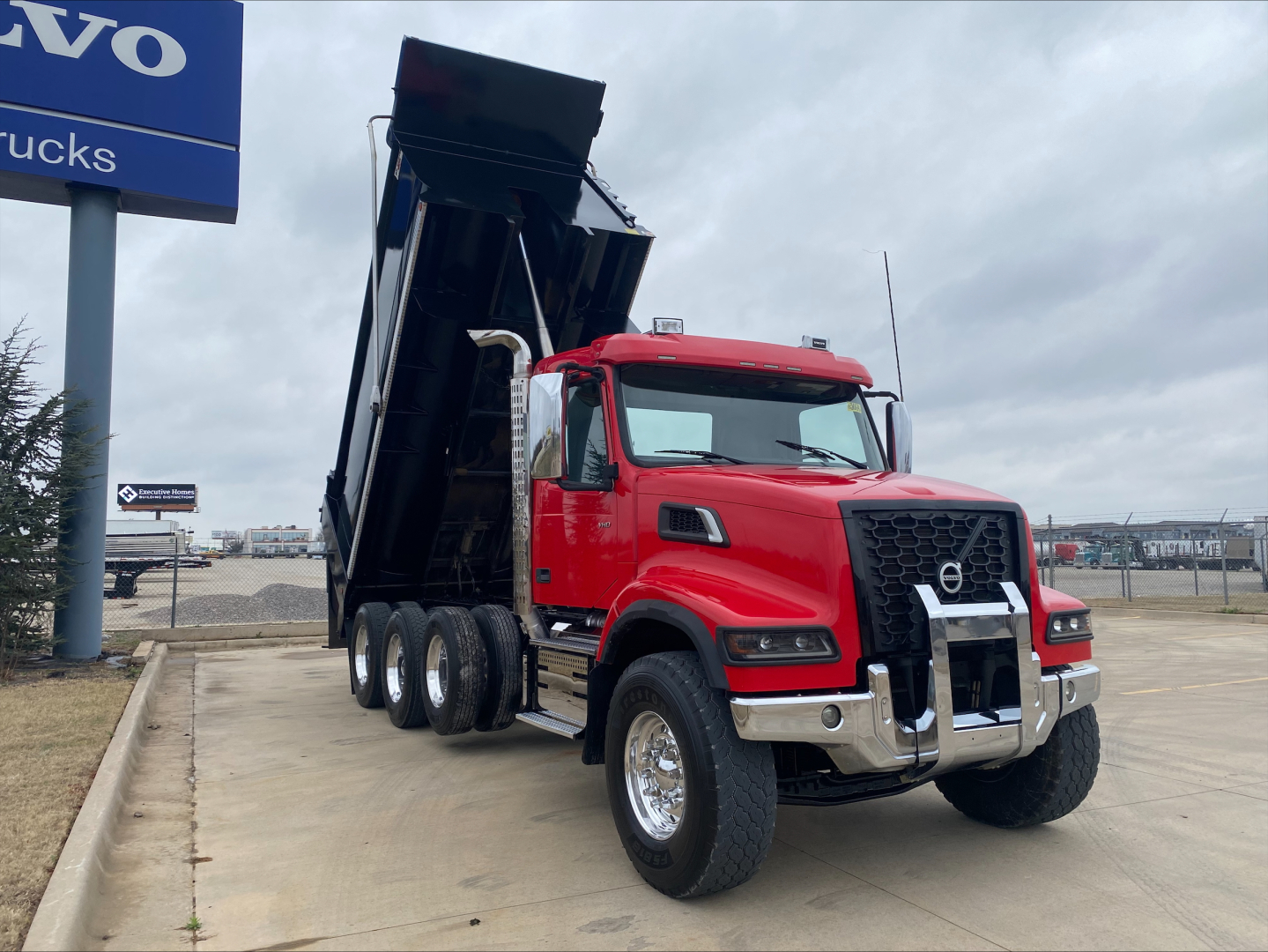 Volvo VHD84F200 dump truck with raised bed, red cab, chrome bumper, black dump body, showing front three-quarter view.