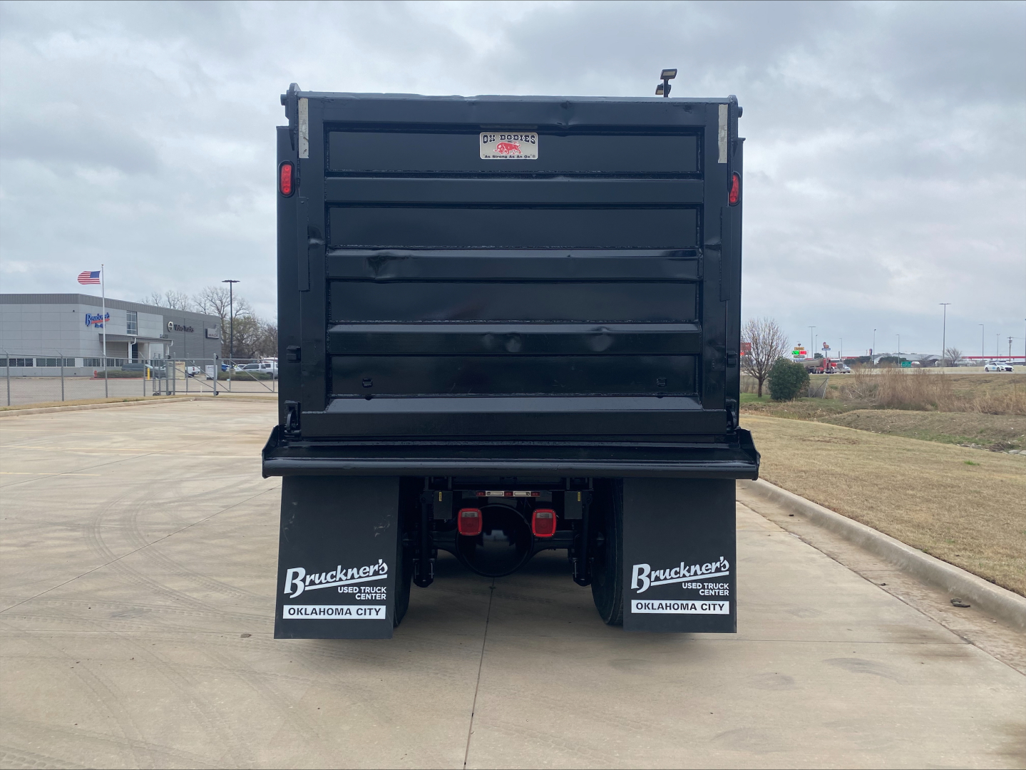 Dump truck bed rear view showing black cargo box and dual rear fender mud flaps with Bruckner’s logos and Oklahoma City text