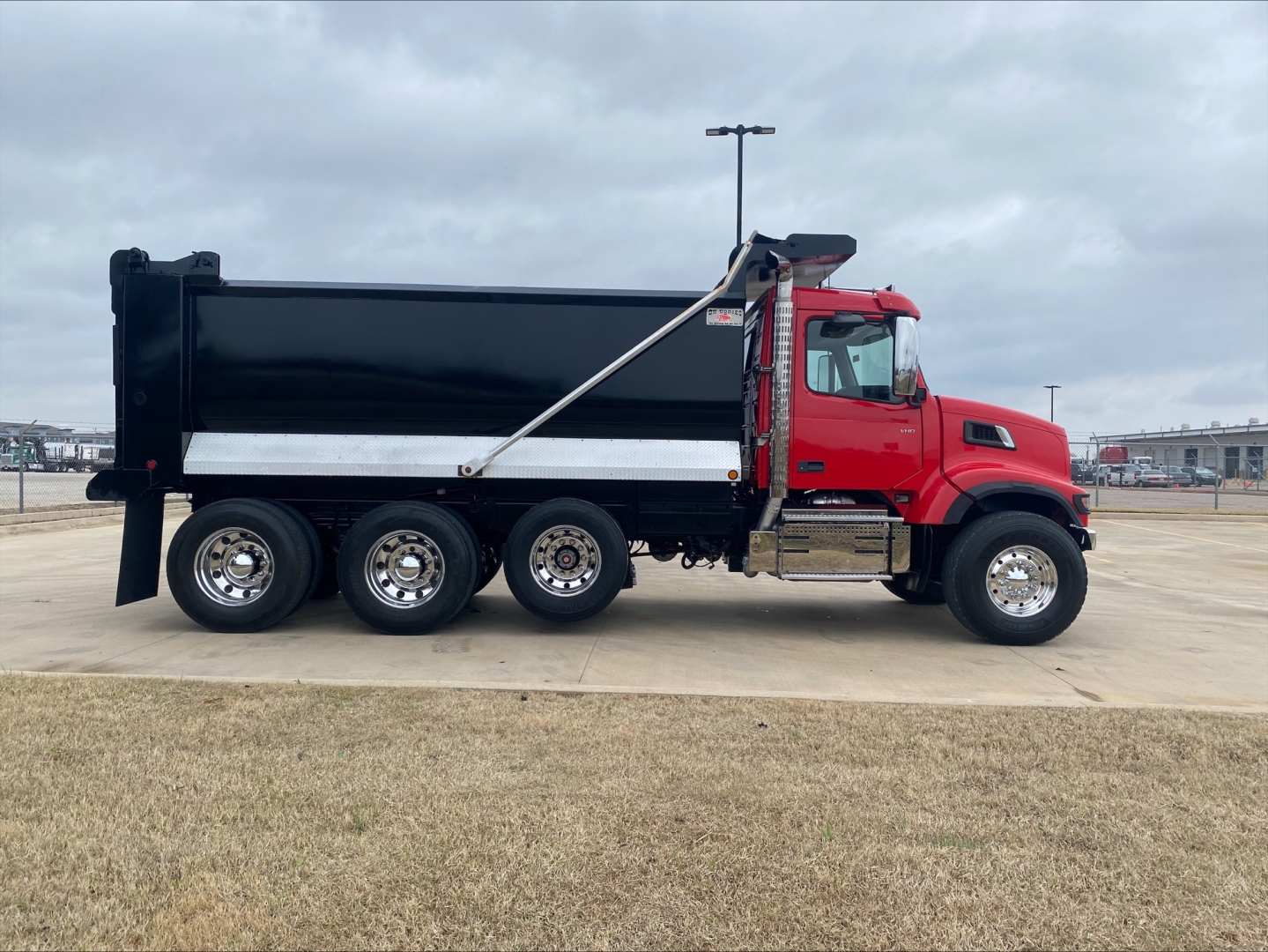 Volvo VHD84F200 dump truck side view showing red cab and black dump bed with chrome steps and dual rear wheels.