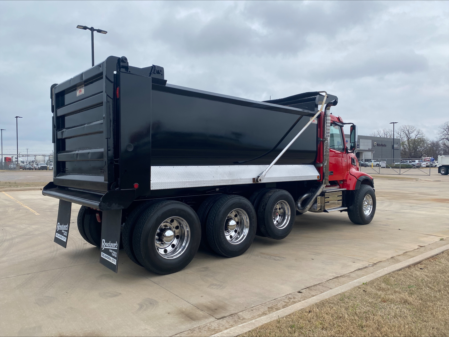 Dump truck with red cab and black dump bed, rear three-axle wheels visible, with sponsor mud flaps and chrome wheels.