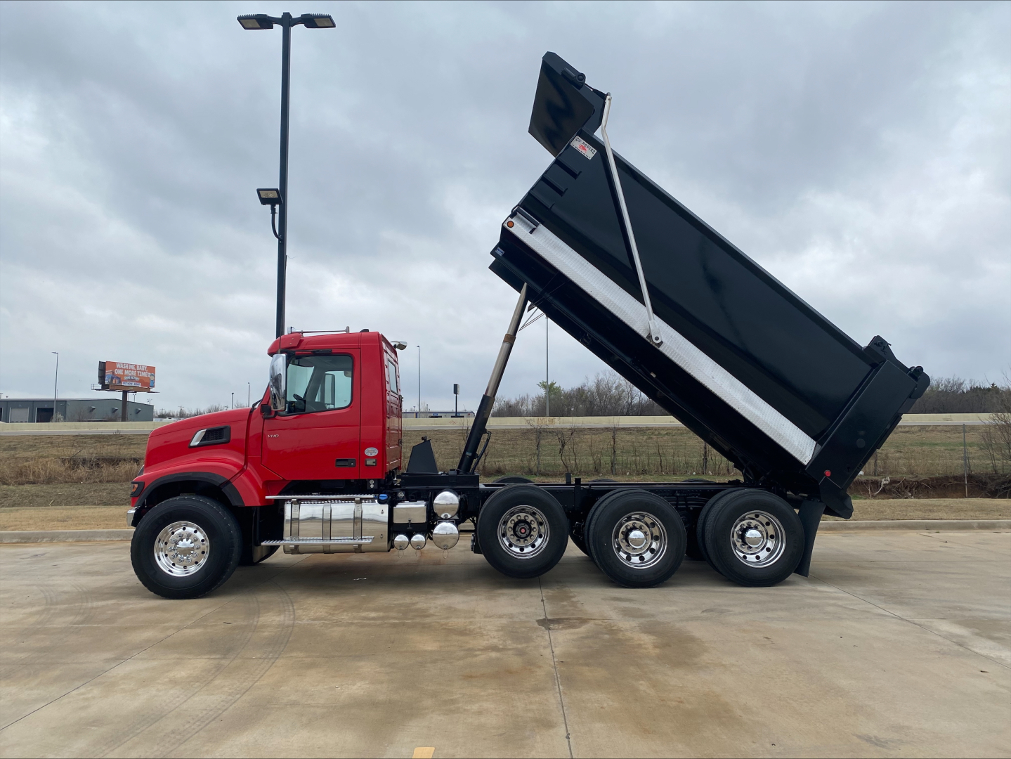 Volvo VHD84F200 dump truck side view with hydraulic dump bed raised, red cab, multiple rear axles, chrome exhaust stacks, and black dump body.