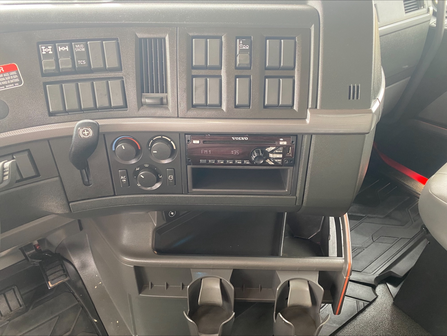 Volvo VHD84F200 truck interior dashboard with climate controls, radio, and storage shelf showing cup holders.