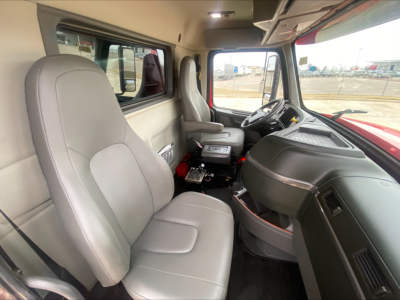 Cab interior of a Volvo VHD truck showing grey cloth seats, steering wheel, dashboard, and center console from the passenger side.