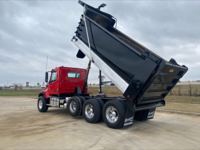 Volvo VHD dump truck with raised black dump bed and red cab, three rear axles, visible side view showing hydraulic lift and dump bed tilt.