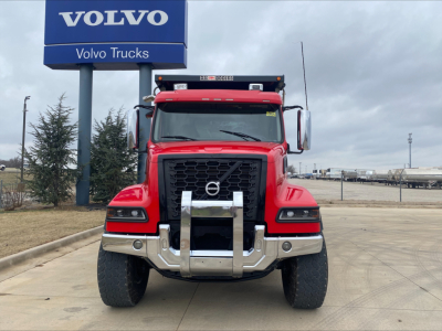 Volvo VHD truck front view in red with large chrome grille guard and bumper, Volvo sign in background, no visible text on truck aside from model features.