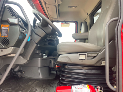 Cab interior of a 2023 Volvo VHD84F200 dump truck showing the driver's seat, steering wheel, dashboard, and floor mat.