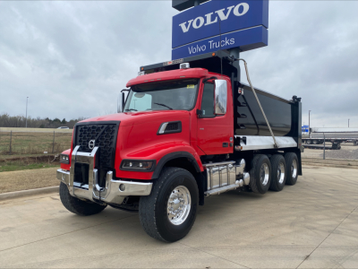 Volvo VHD84F200 dump truck in red cab with black dump body, chrome bumper and wheels, Volvo Trucks sign in background.